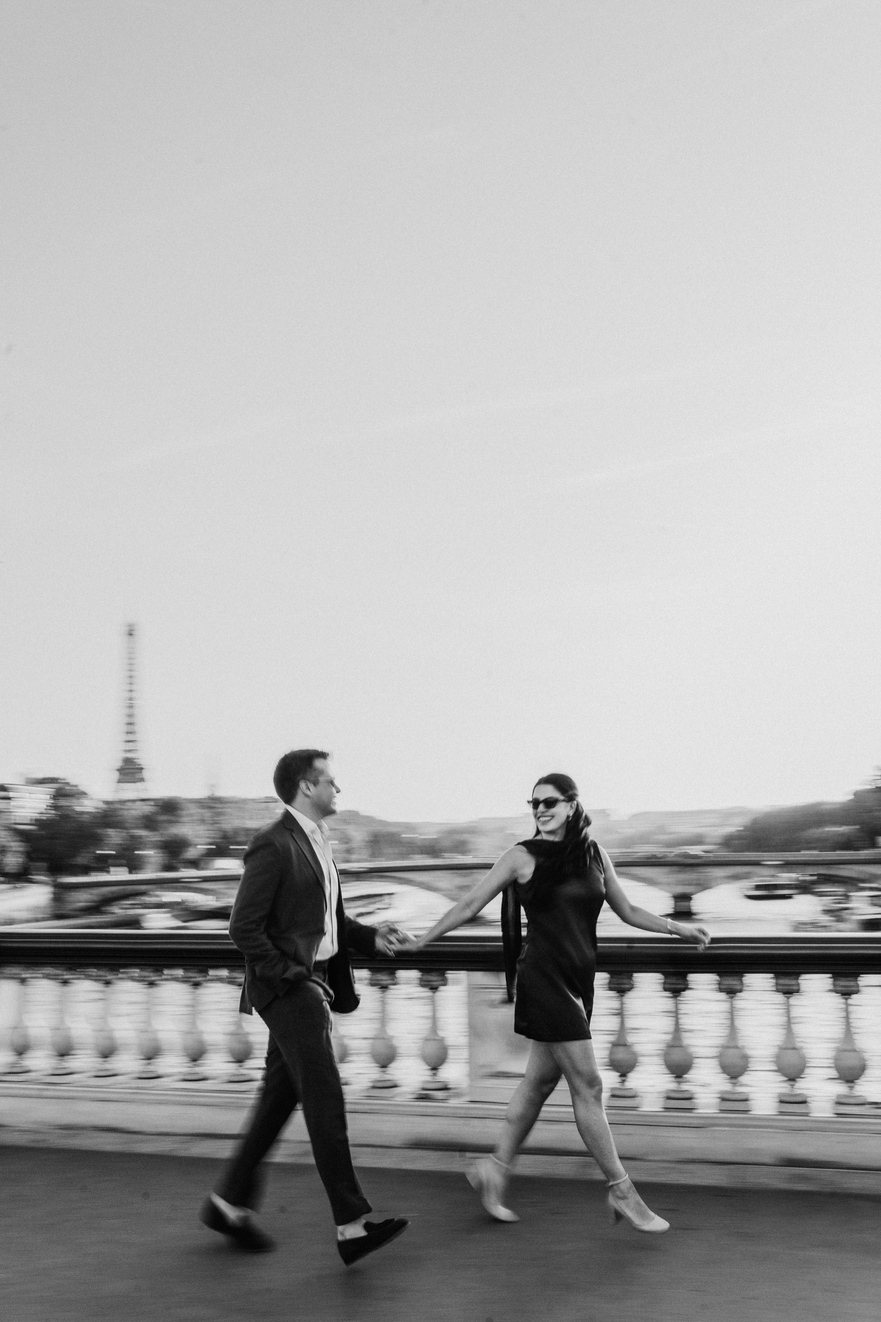 Nada and Seamus walking hand in hand across a Seine bridge in Paris, the Eiffel Tower behind them